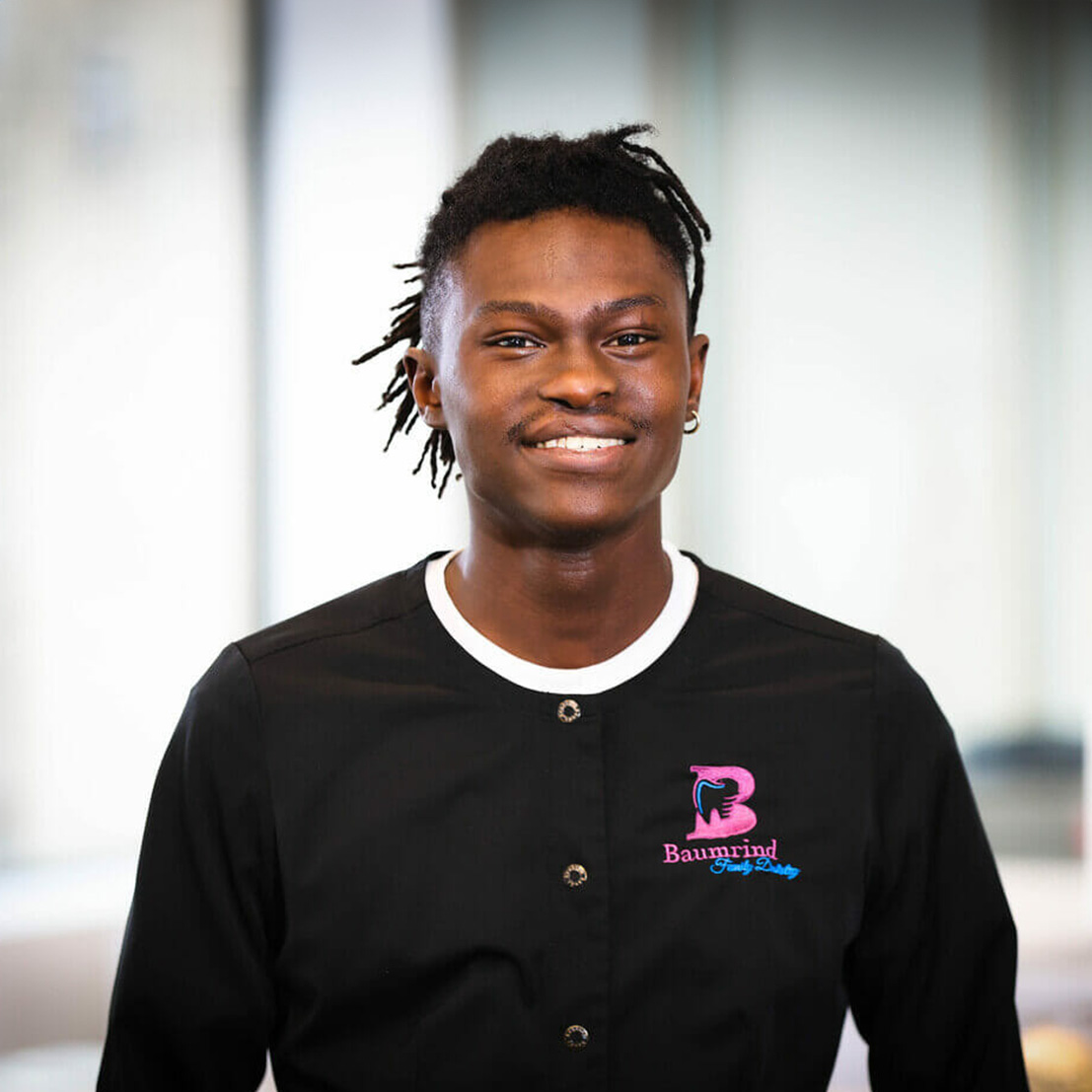 A man wearing a black apron with white text, standing in front of a window.
