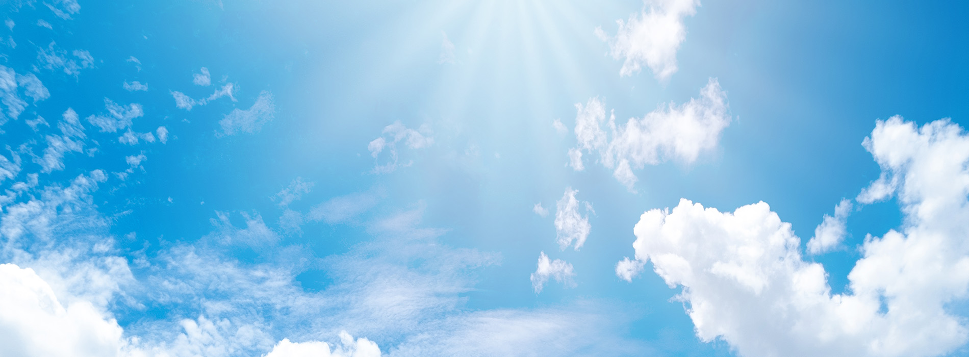 The image shows a bright blue sky with scattered clouds, viewed from below as if looking up at the sun.