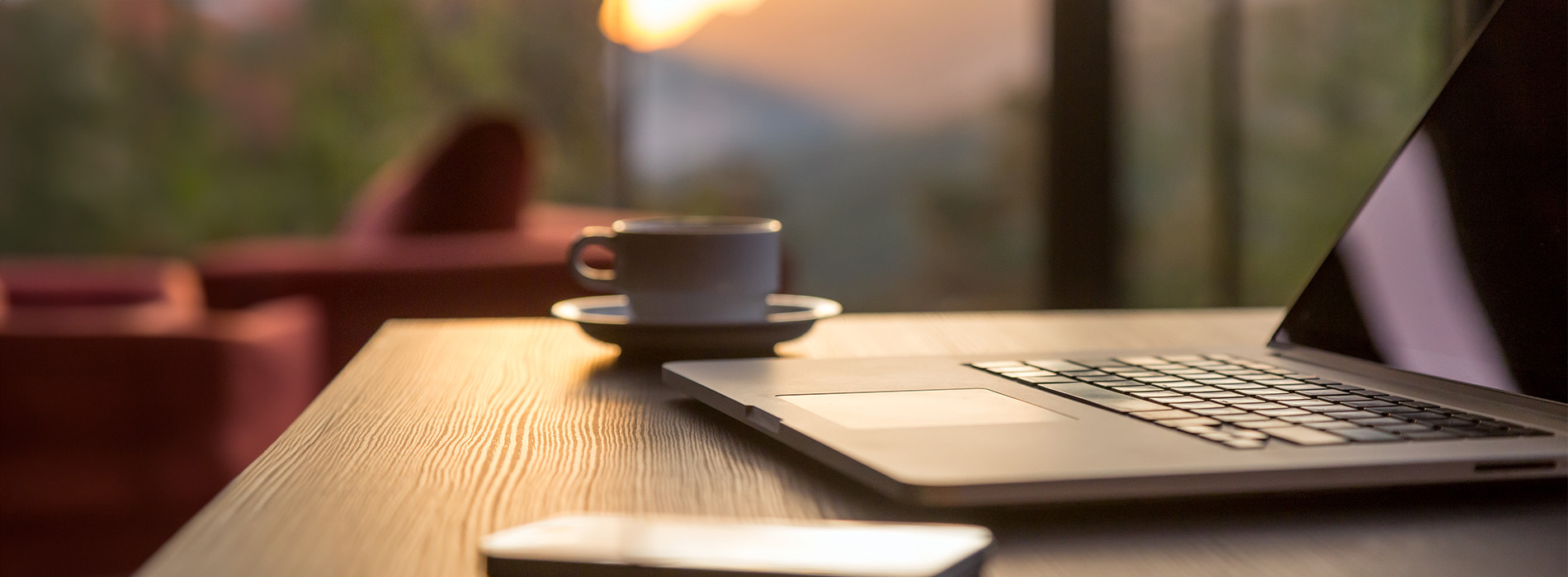 An image of a laptop on a table with a person's hands in the foreground, set against an outdoor background during sunset.