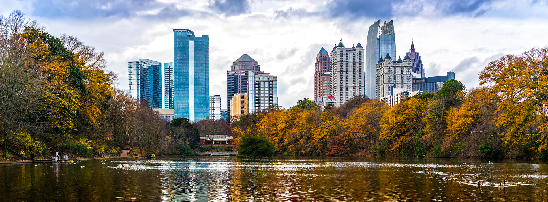 Aerial view of a city skyline with prominent buildings, set against a backdrop of autumnal trees and a river.