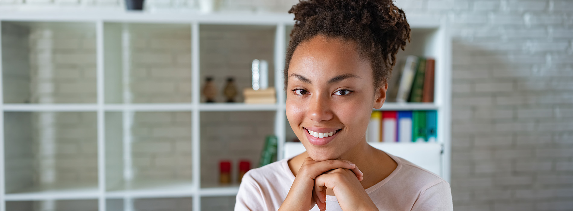 A young woman with a radiant smile stands in a kitchen, her hands clasped together.