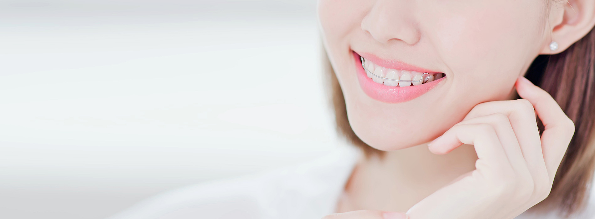 A close-up of a smiling woman with short hair, wearing makeup and earrings, against a blurred background.