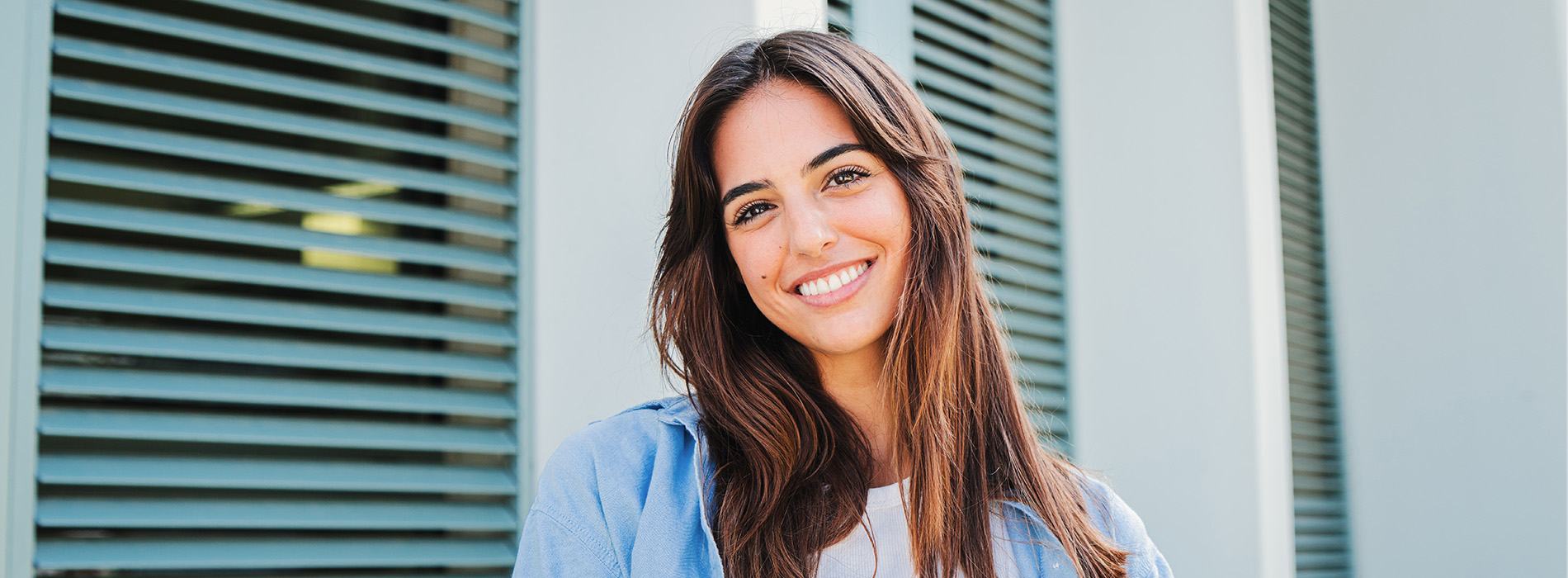 A woman with long hair and a blue top is smiling at the camera.