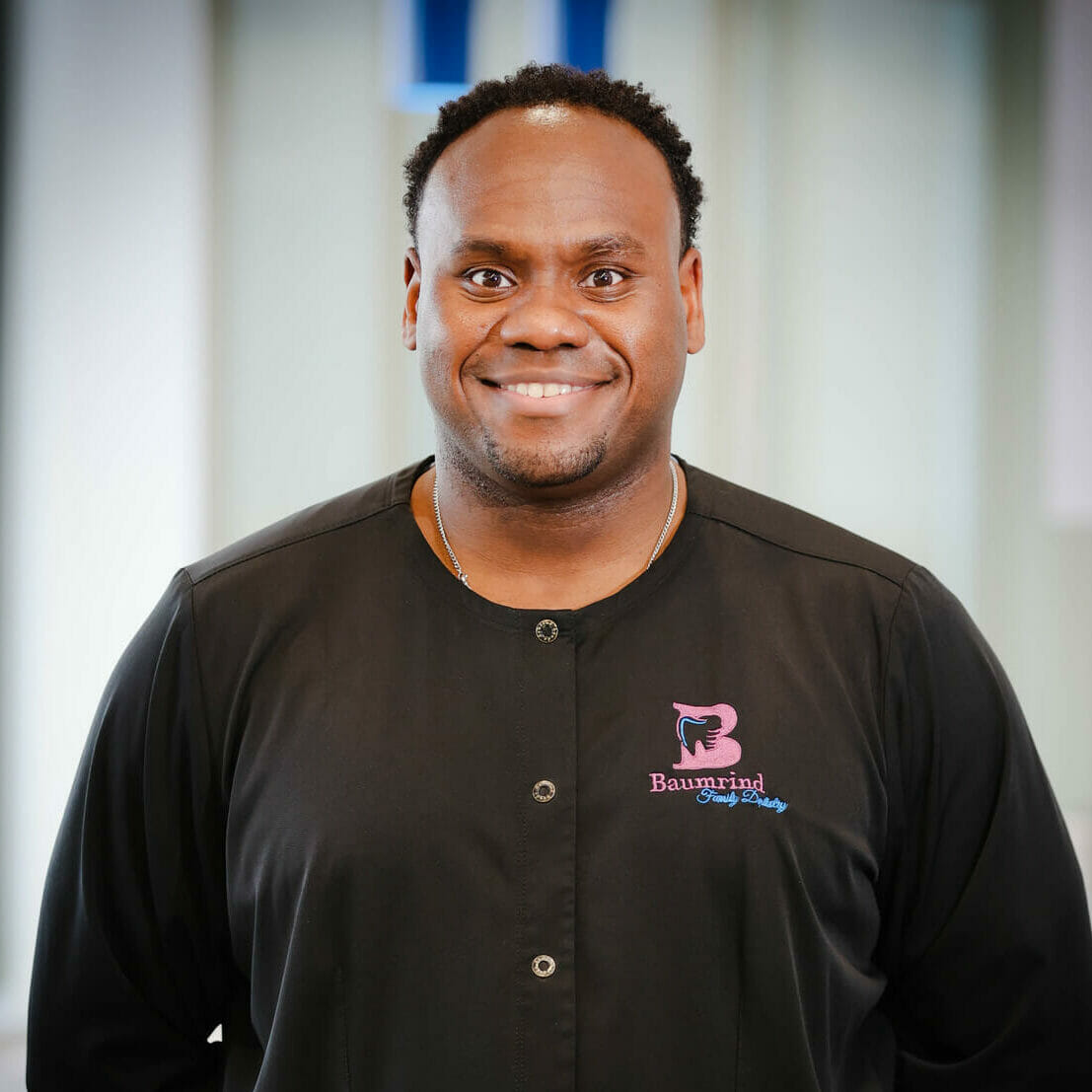 The image shows a man wearing a black jacket with the name  BAMBI  on it, standing in front of a blue and white sign. He is smiling and appears to be posing for the photograph.