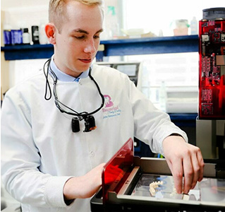 A man in a white lab coat with blonde hair is standing behind a counter, examining an object with his hands.