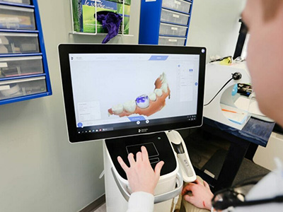 The image shows a person using a computer screen to view a 3D model of a human tooth, likely in a dental or medical setting, with the focus on the digital display.