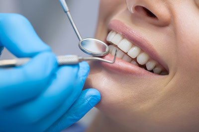 The image shows a person receiving dental care, with a dental professional working on their teeth using specialized tools.