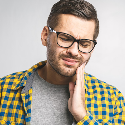 Man with glasses, beard, and mustache wearing a plaid shirt and holding his hand to his mouth.