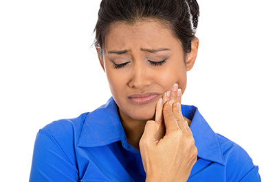 A woman with a concerned expression, holding her face and looking downwards with her mouth slightly open.