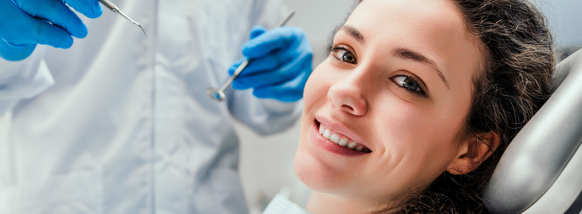 The image shows a person receiving dental care, with a dentist or dental hygienist working on their teeth while they are seated in the dental chair.