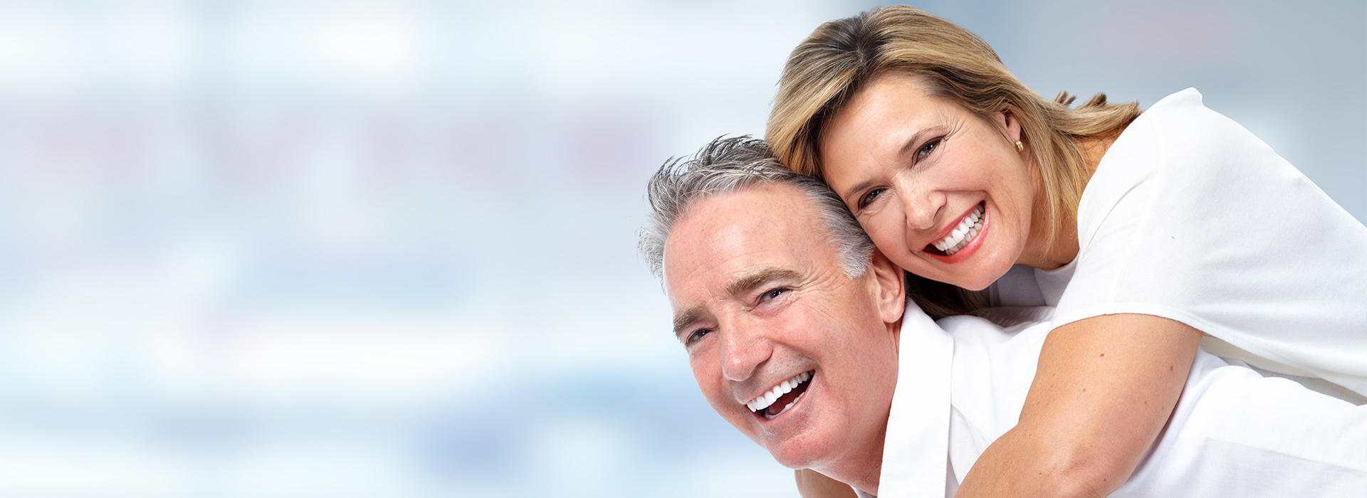 A man and a woman, both smiling, embracing in front of a blurred background.