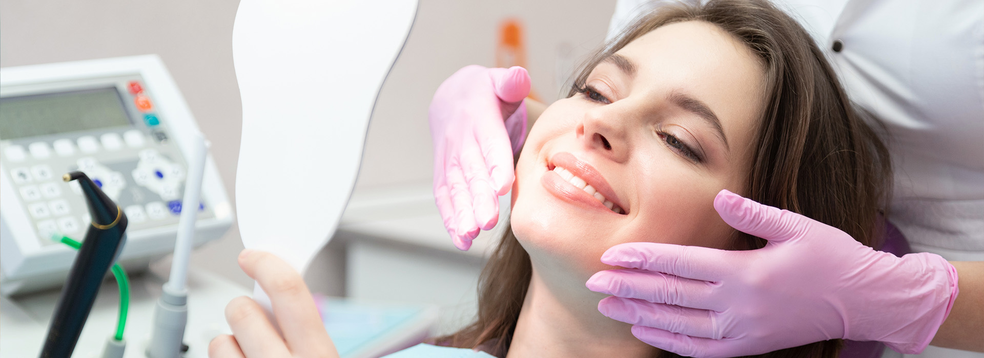 A woman is sitting in a dental chair, receiving dental care from a professional wearing gloves and a mask.