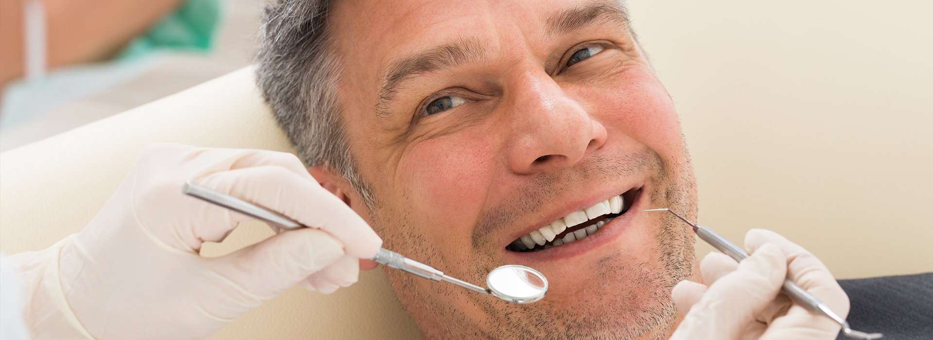 A man receiving dental treatment in a clinical setting, with a dentist using tools and wearing gloves.