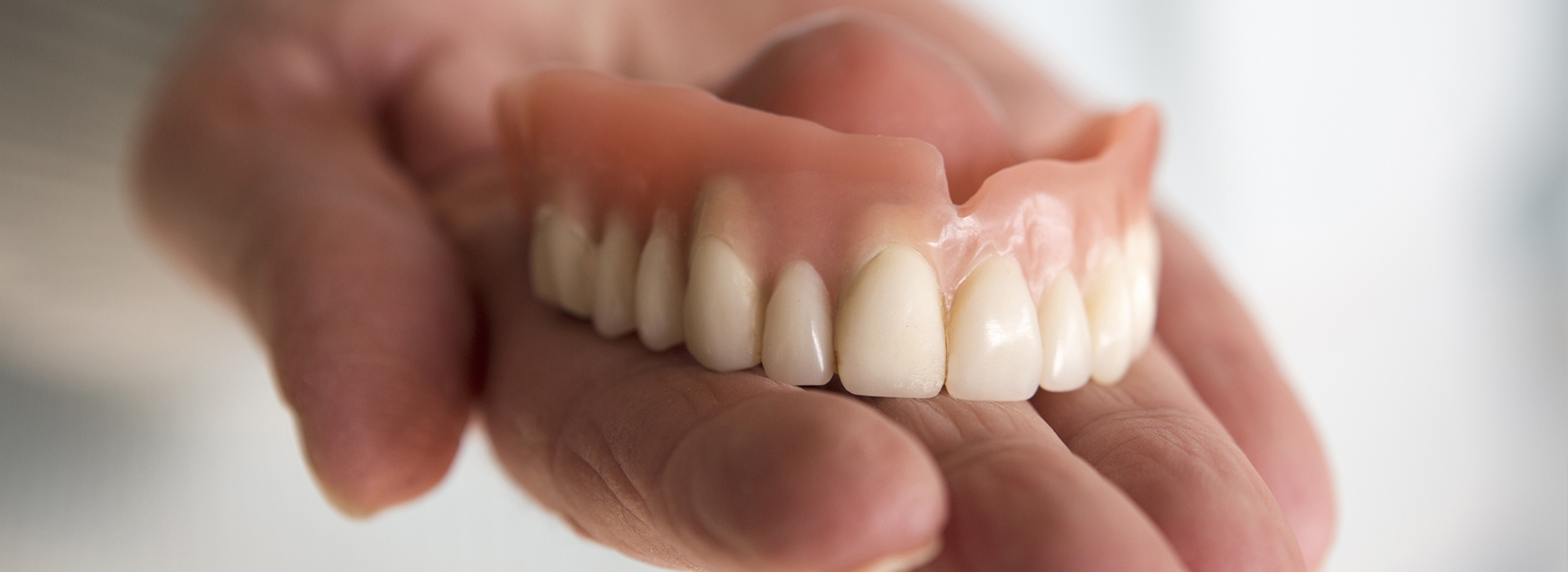 A hand holding a set of dentures with an open mouth, showcasing the false teeth.