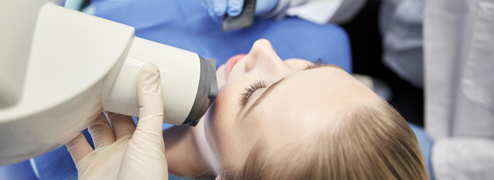 A woman receiving a dental implant procedure, with a dental implant in progress and a medical professional operating the equipment.