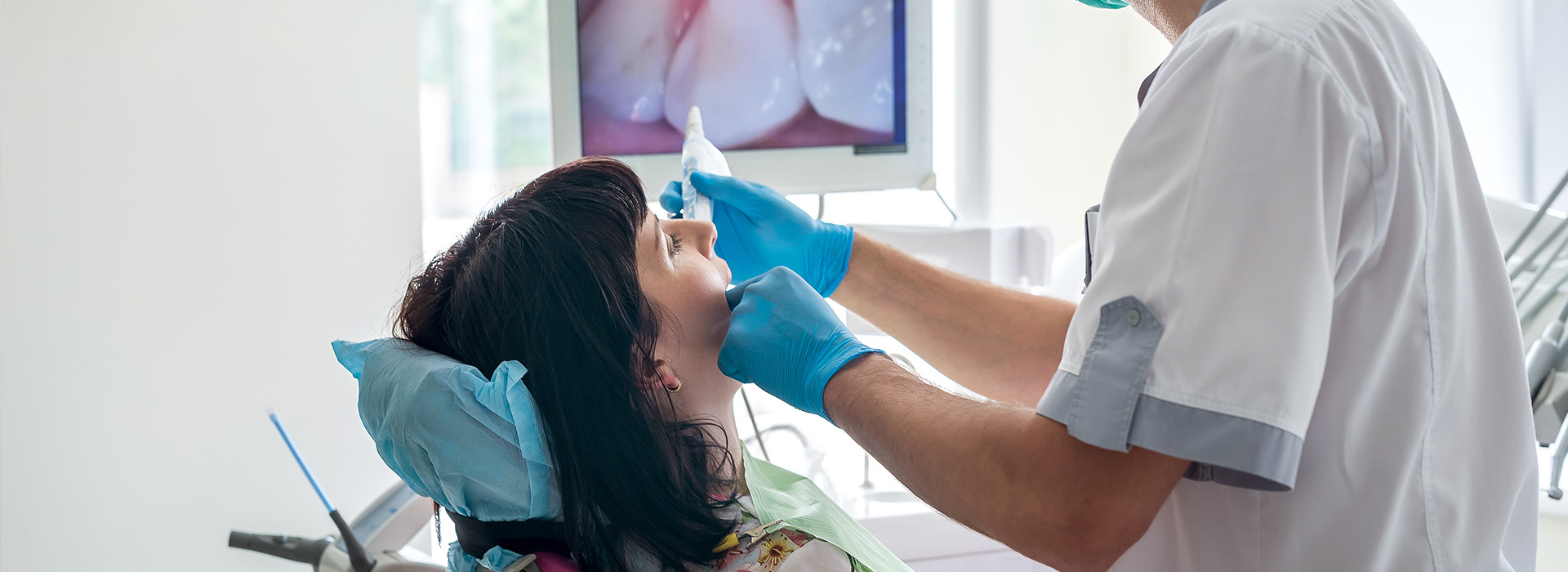 A dental hygienist is performing a cleaning procedure on a patient s teeth, with the dentist sitting in front of a large screen displaying an image of a mouth.