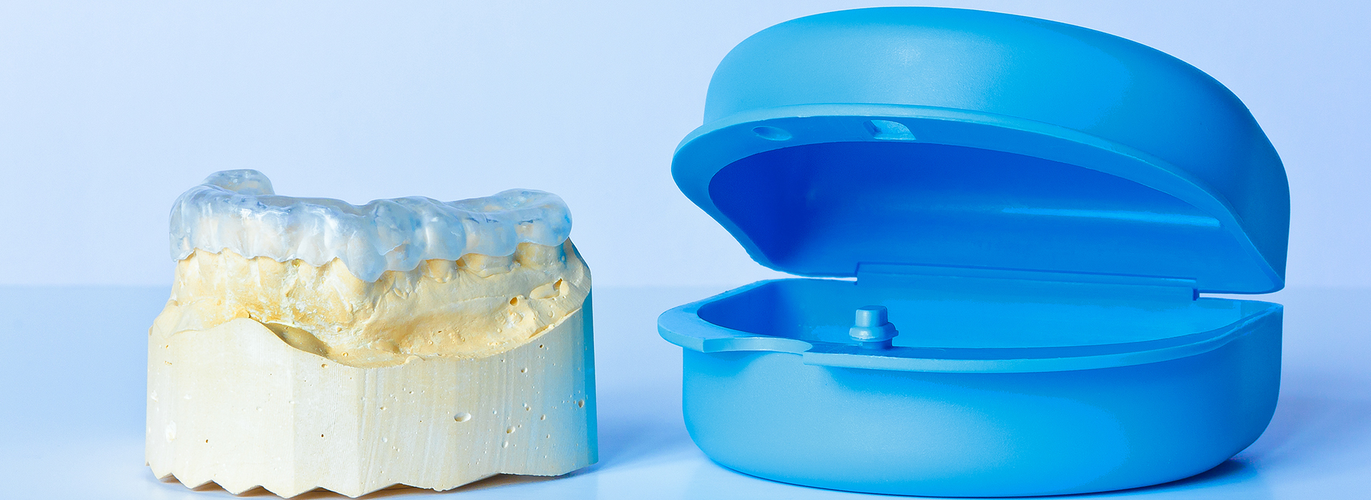 The image displays a pair of blue dental models and a yellow model of a human tooth, placed side by side against a white background.