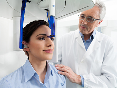 A woman is seated in a dental chair, receiving dental treatment from a professional who is standing next to her.