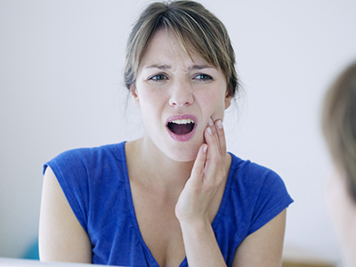 The image shows a woman with her mouth open, displaying teeth, in front of a mirror. She appears to be expressing surprise or shock.