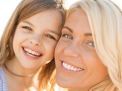 A woman and a young girl smiling at the camera, with the woman s face partially obscured by her hair.