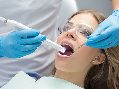 The image shows a woman in a dental chair receiving dental treatment, with a dental professional using a device to examine her teeth.