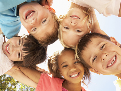 A group of six children, three boys and three girls, smiling at the camera with their arms around each other.