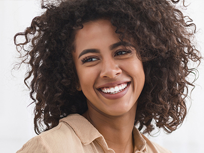 Smiling woman with curly hair, wearing a brown top and earrings, against a white background.